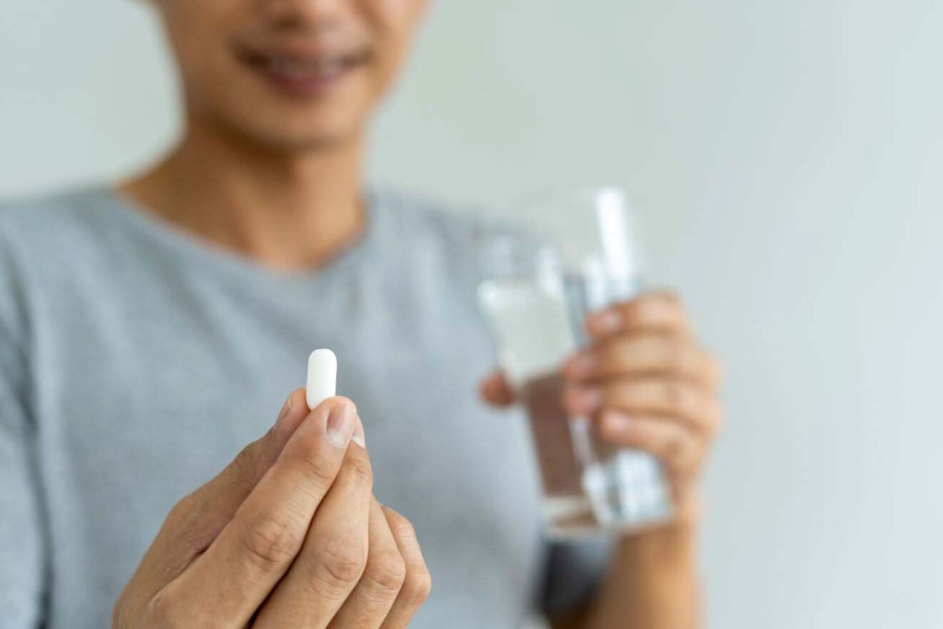 A person holding a pill in one hand and a glass of water in the other.