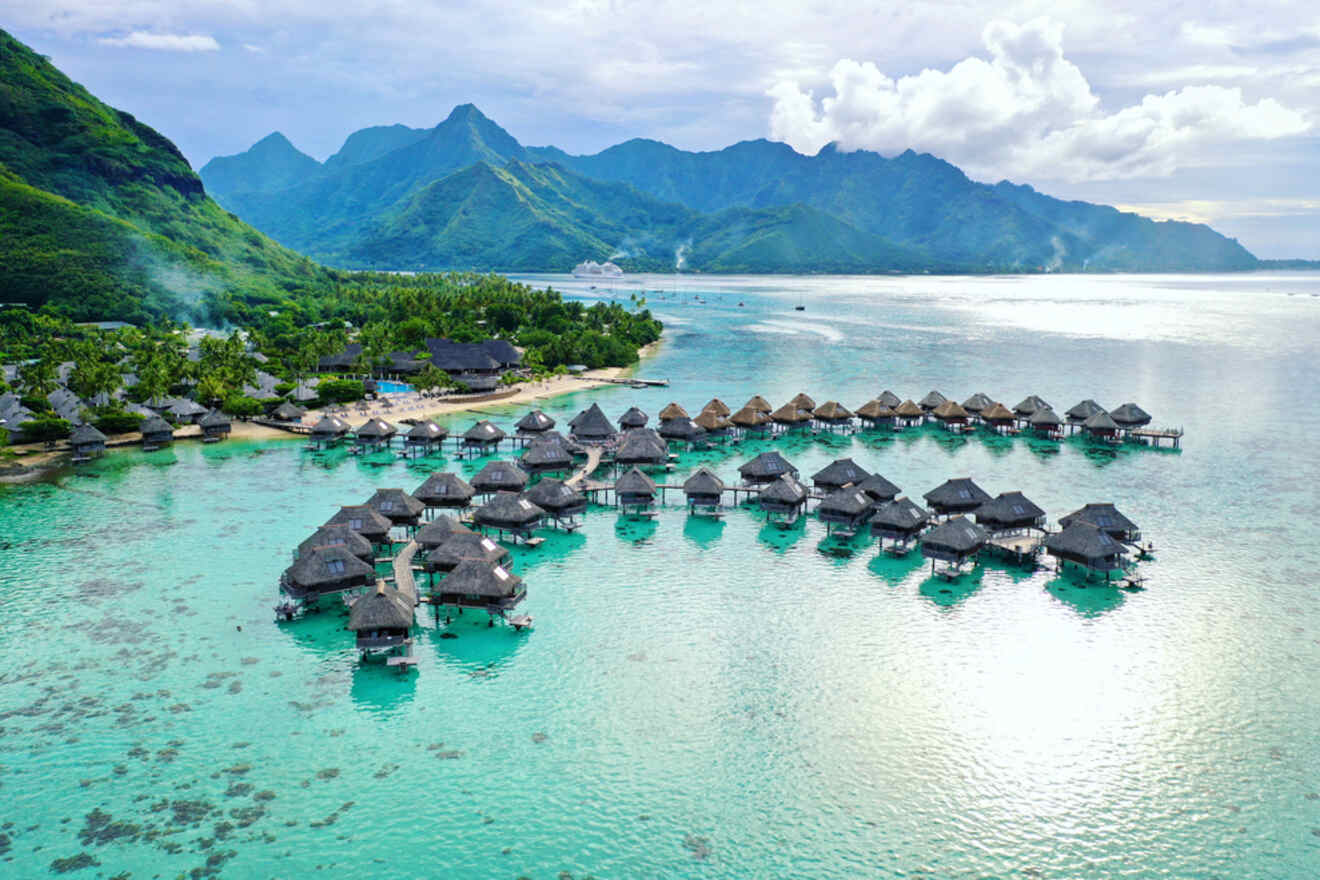 Overwater bungalows in a turquoise lagoon with lush mountains in the background on the island of Moorea.