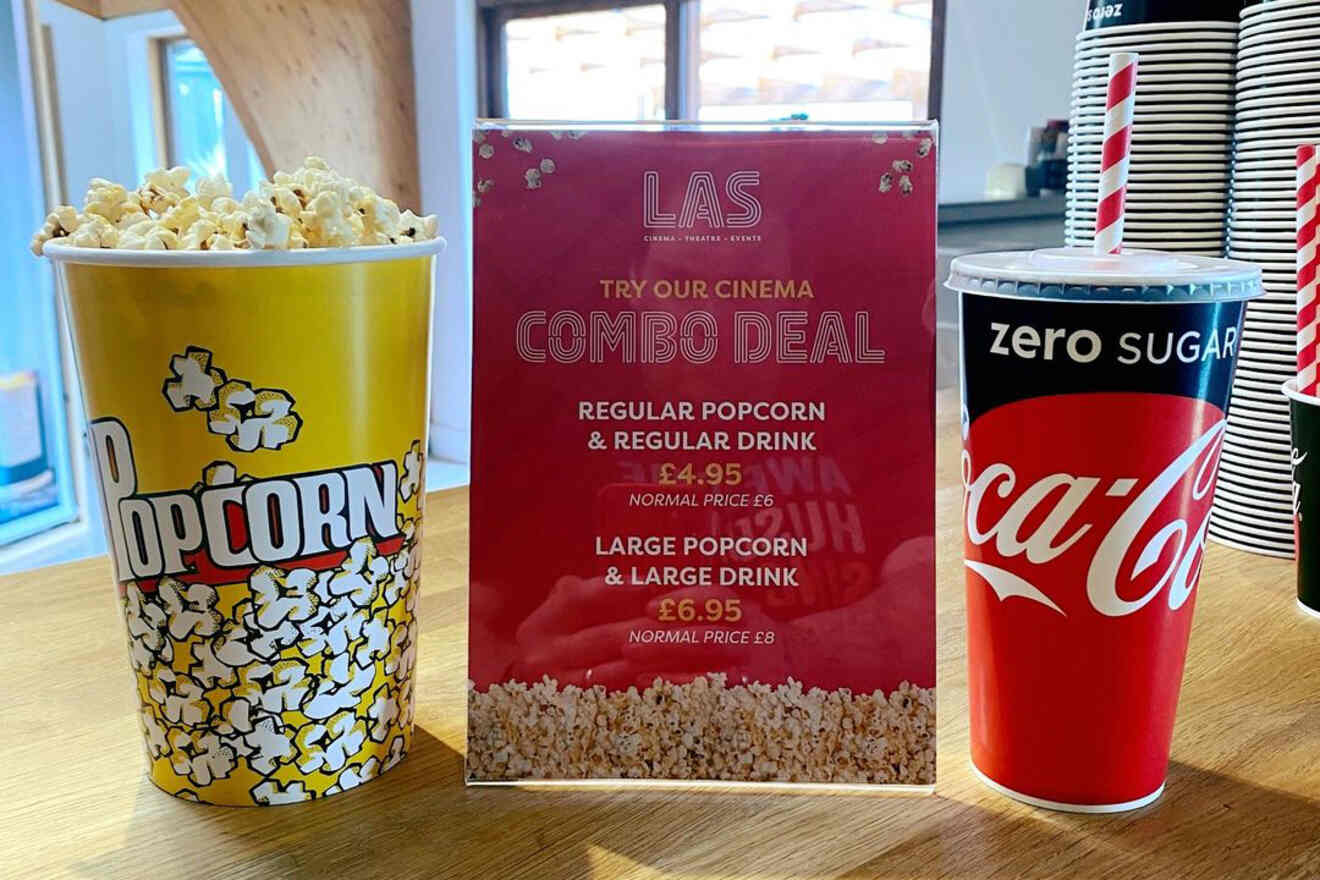 A box of popcorn, a combo deal sign, and a zero sugar Coca-Cola cup are displayed on a wooden counter at a cinema.