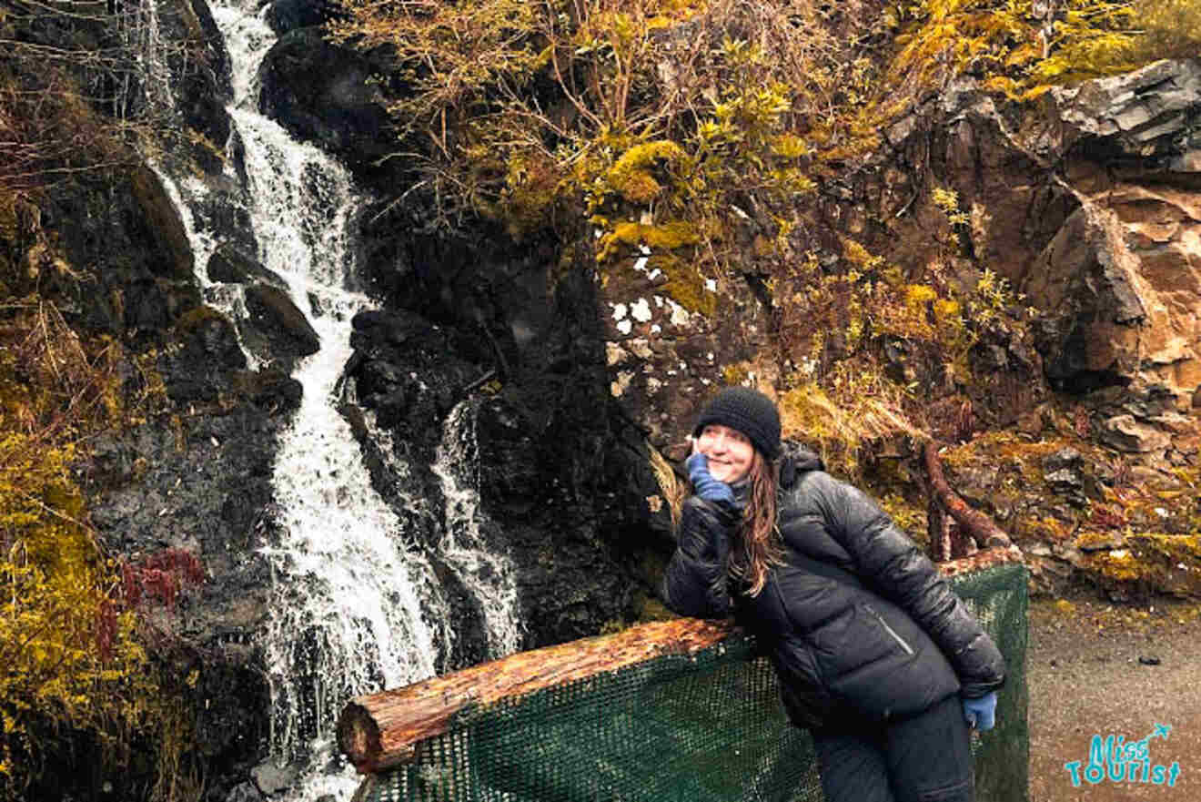 The writer of the post smiling next to a waterfall at Dunvegan Castle, wearing a black winter coat and hat.