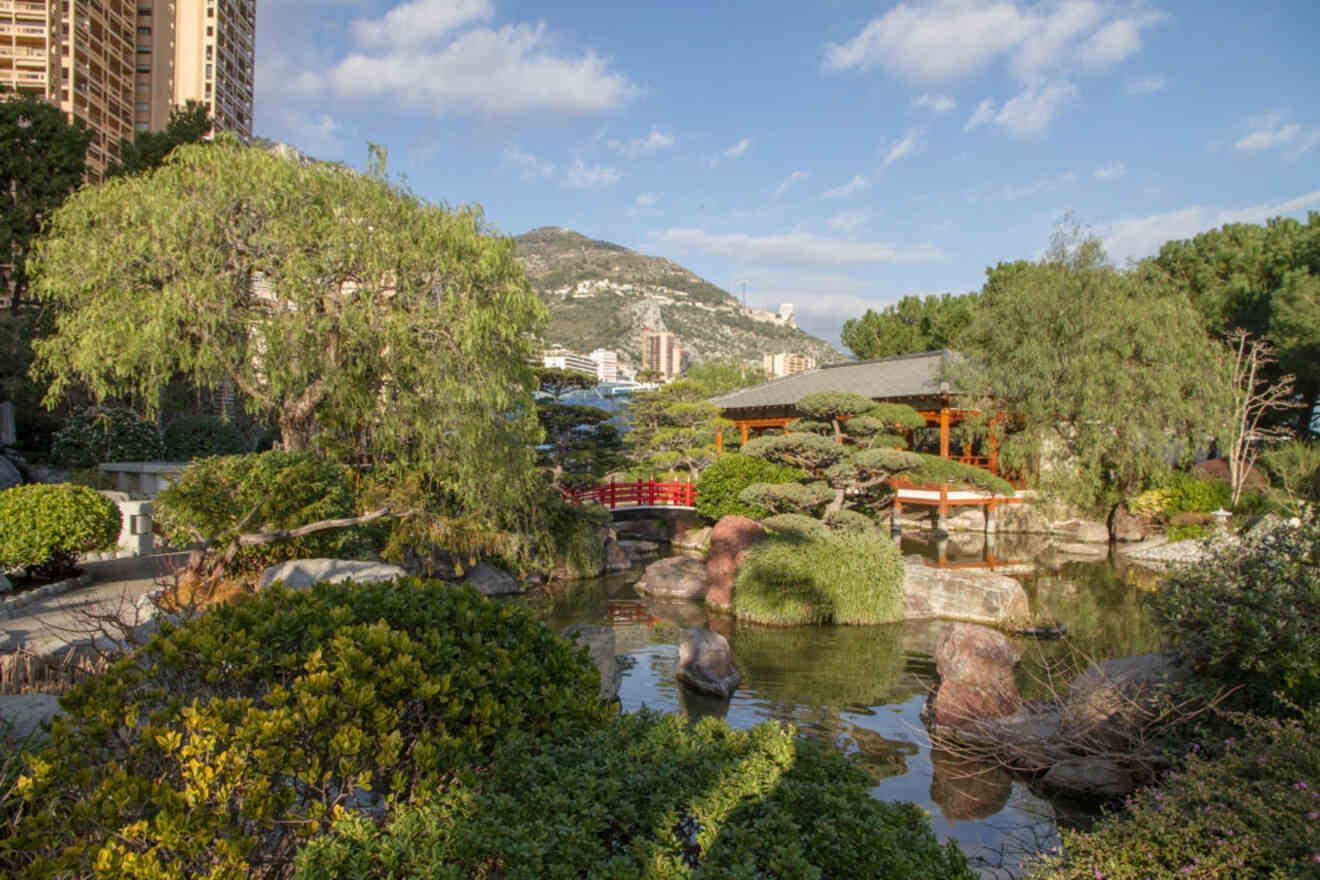 A serene Japanese garden with traditional architecture, a red bridge, and lush greenery, located in Monaco.