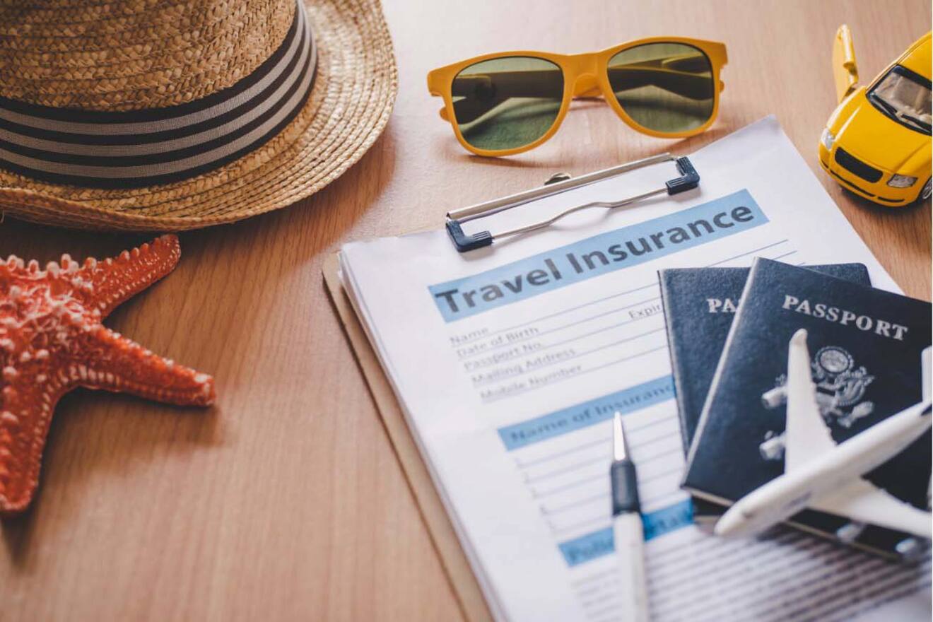 A travel insurance form on a table next to a hat, sunglasses, passports, and a toy airplane.