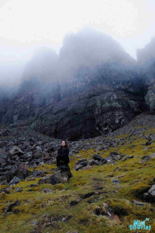 The writer of the post standing in a misty, rocky landscape at the base of a mountain, looking up towards the fog-covered peak.