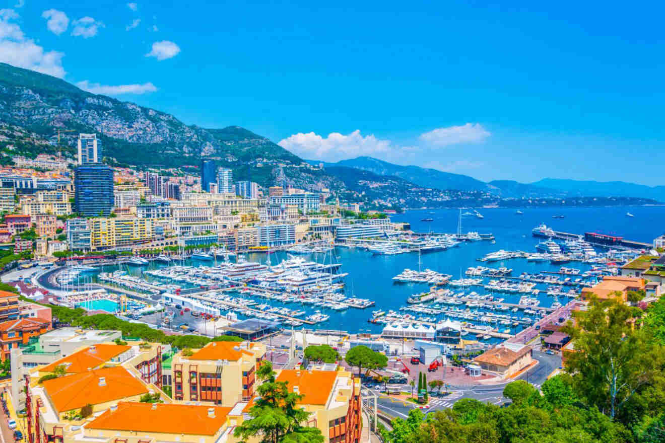 A vibrant marina filled with yachts, set against the backdrop of Monaco's colorful buildings and mountainous landscape.