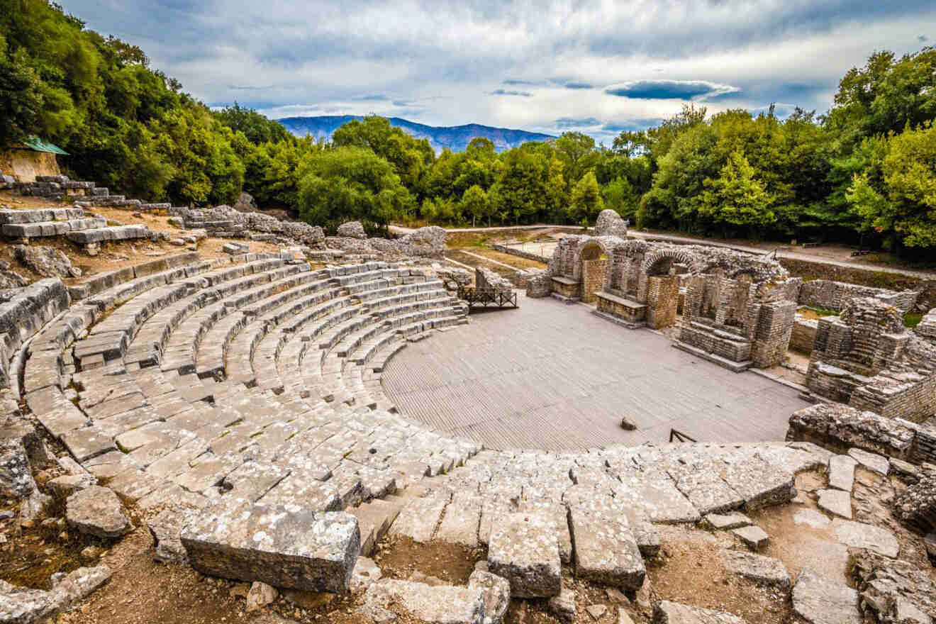 The ancient amphitheater in Butrint National Park, surrounded by lush greenery and ruins.