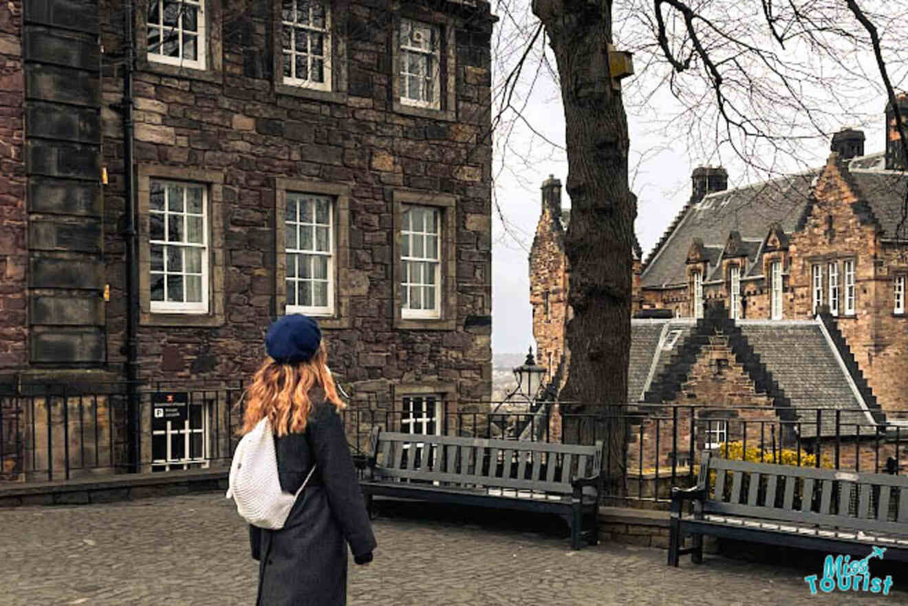 The writer of the post looking at historic buildings in a courtyard, with benches and bare trees in Edinburgh