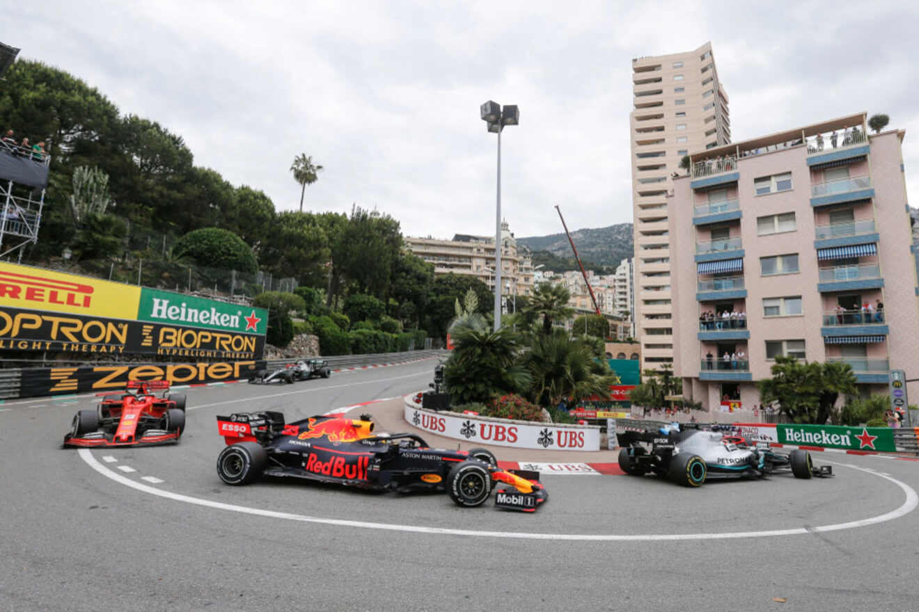 Formula 1 cars navigating a tight turn during the Monaco Grand Prix, with spectators watching from nearby buildings.