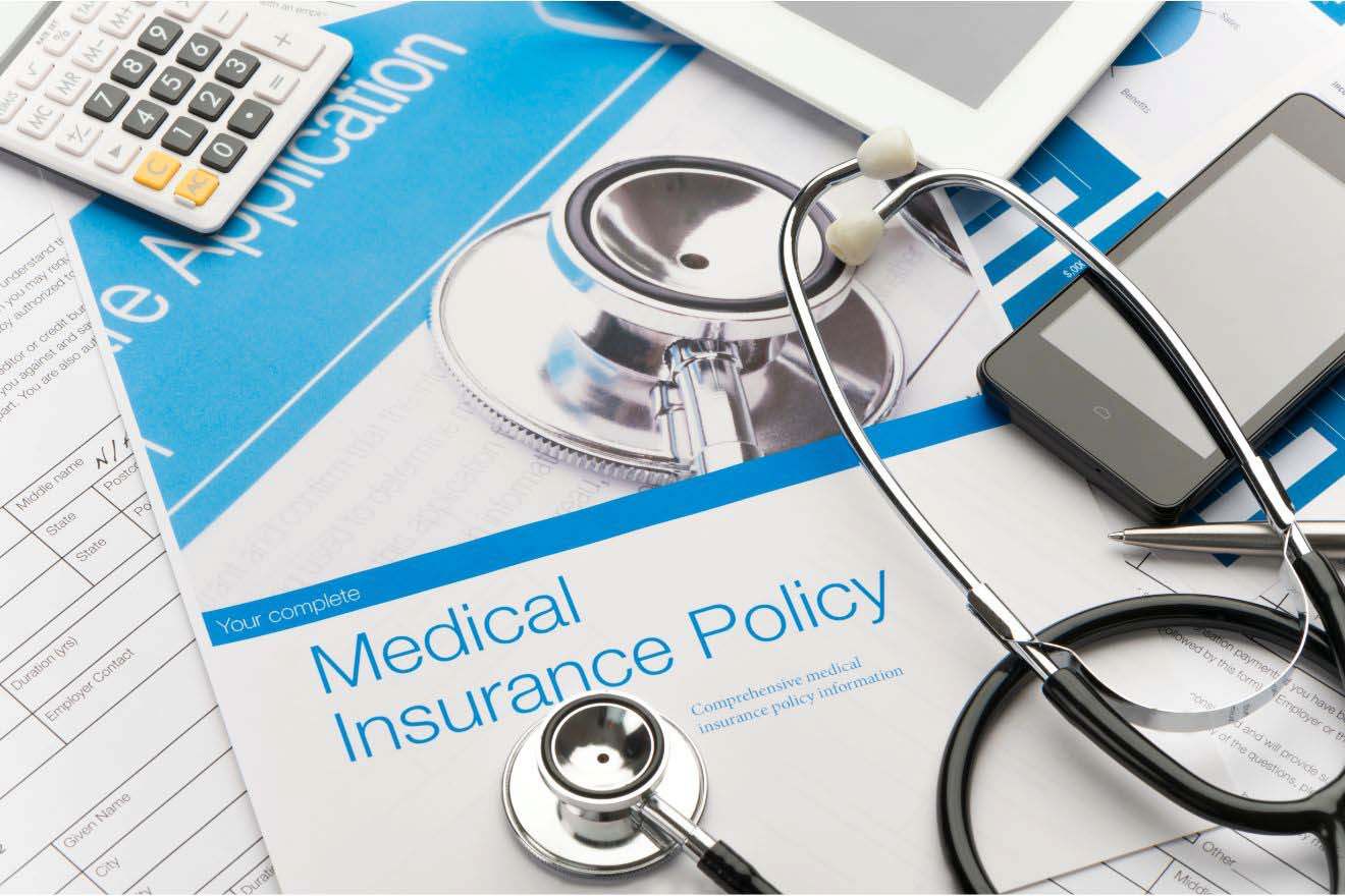 A medical insurance policy document on a table alongside a stethoscope, a calculator, and a smartphone.