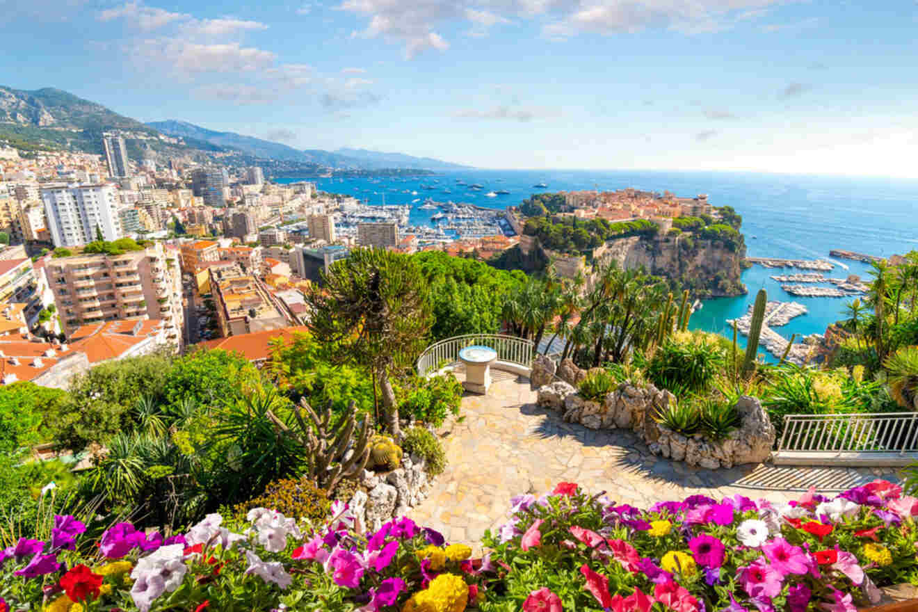 A vibrant garden filled with colorful flowers and lush greenery, overlooking the scenic cityscape and coastline of Monaco.