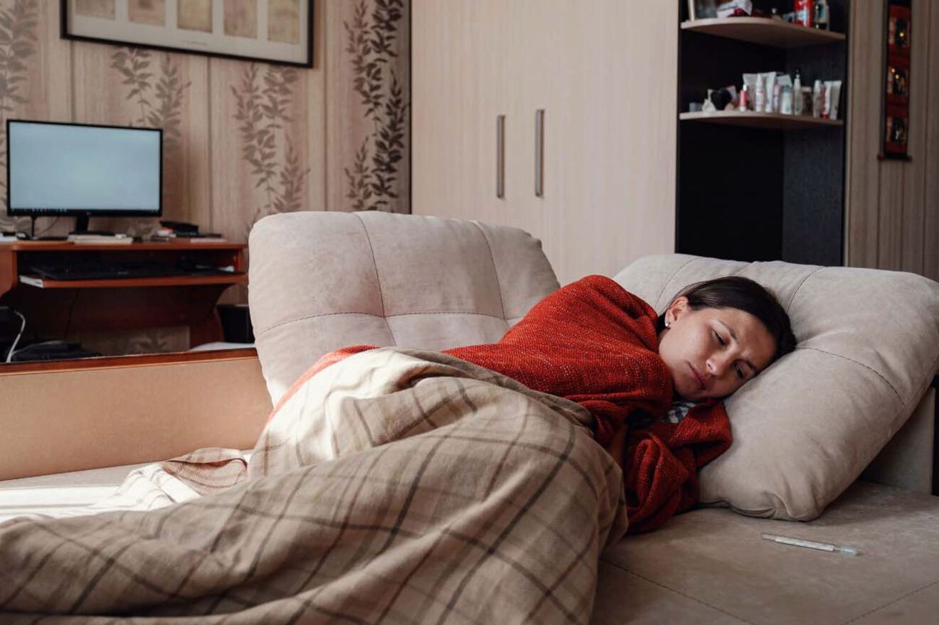 A woman lying on a couch under a blanket, appearing to rest or sleep.