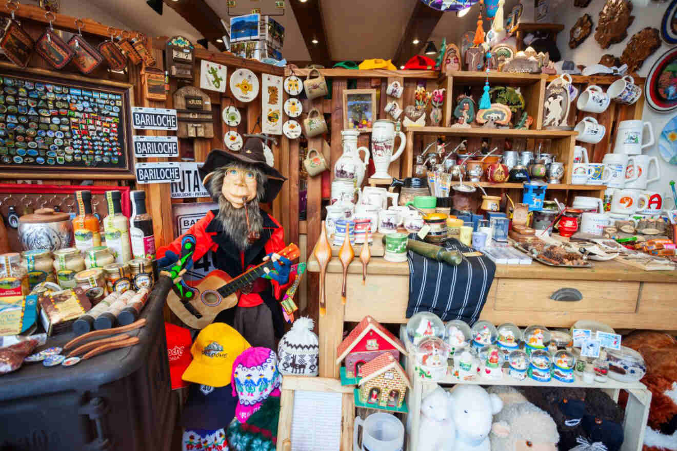 A crowded souvenir shop filled with various items, including mugs, magnets, and a puppet dressed as a musician, with colorful displays on shelves.