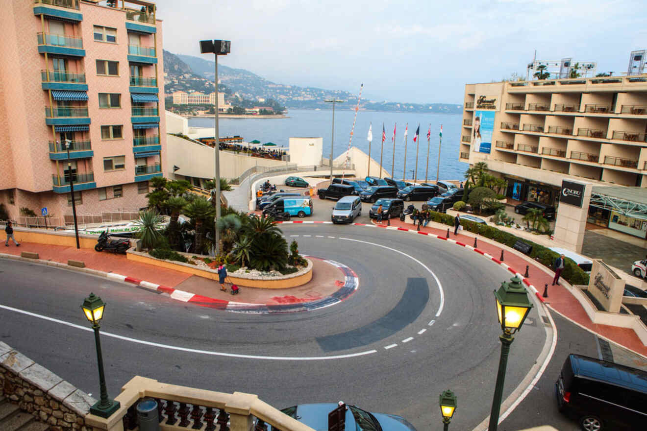 A section of the Monaco Grand Prix circuit with a sharp turn, surrounded by residential buildings and luxury cars parked nearby.