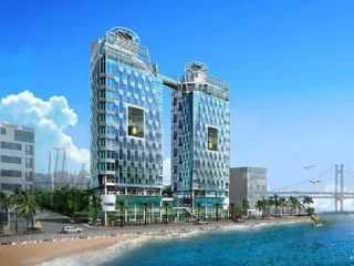 Twin high-rise buildings with glass facades overlooking a beach, connected by a skybridge.