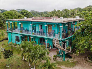 A two-story turquoise building with a spiral staircase, balconies, and surrounding greenery.