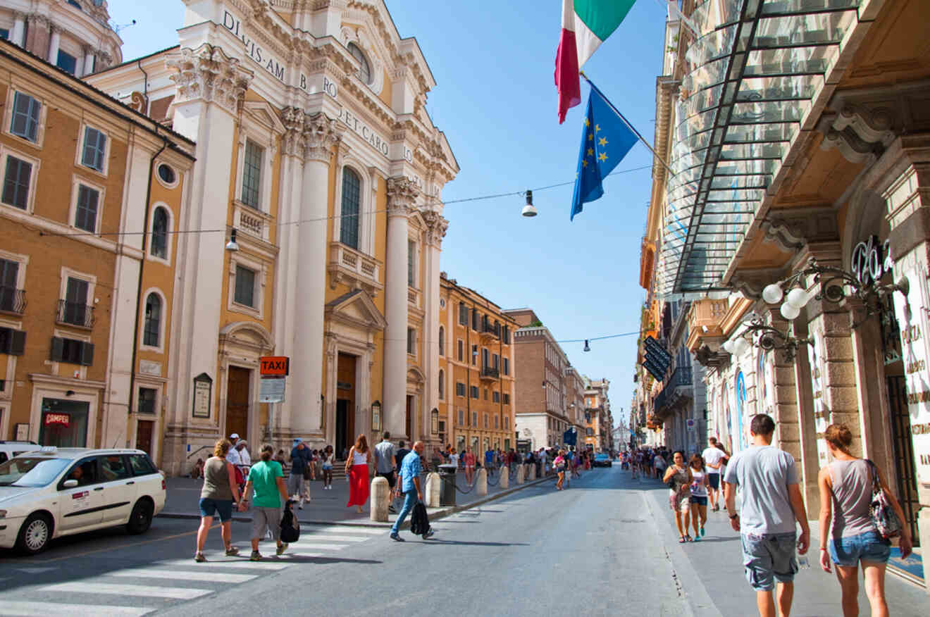 A bustling street in Rome with people walking, cars passing, and the beautiful facade of a historic church.