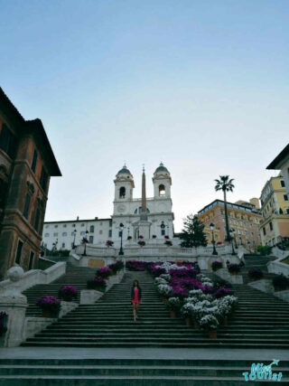 The writer of the post standing on the Spanish Steps in Rome, surrounded by colorful flowers and historic buildings.