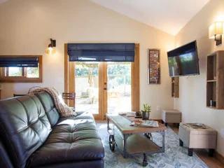 A cozy living room with a black leather sofa, a modern coffee table, a mounted TV, and a view of the patio through glass doors.
