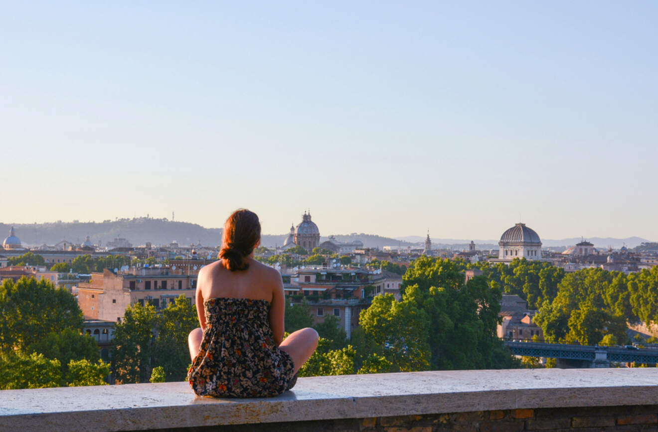 A person sitting on a ledge, admiring the panoramic view of Rome's skyline at sunset.