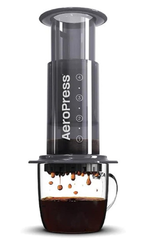 A transparent AeroPress coffee maker with dark coffee being brewed into a clear glass mug below.