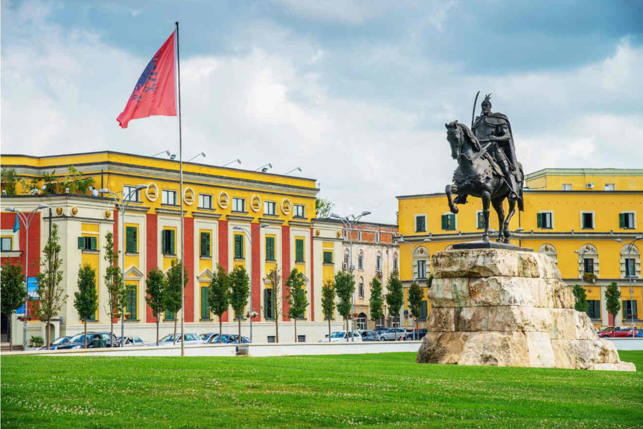 The Skanderbeg statue in Tirana's main square, with colorful buildings and the Albanian flag in the background.