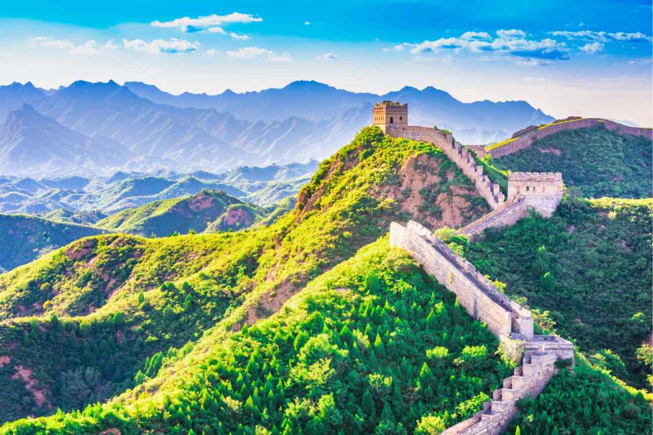 Stretch of the Great Wall of China winding through lush green mountains with a clear sky overhead.