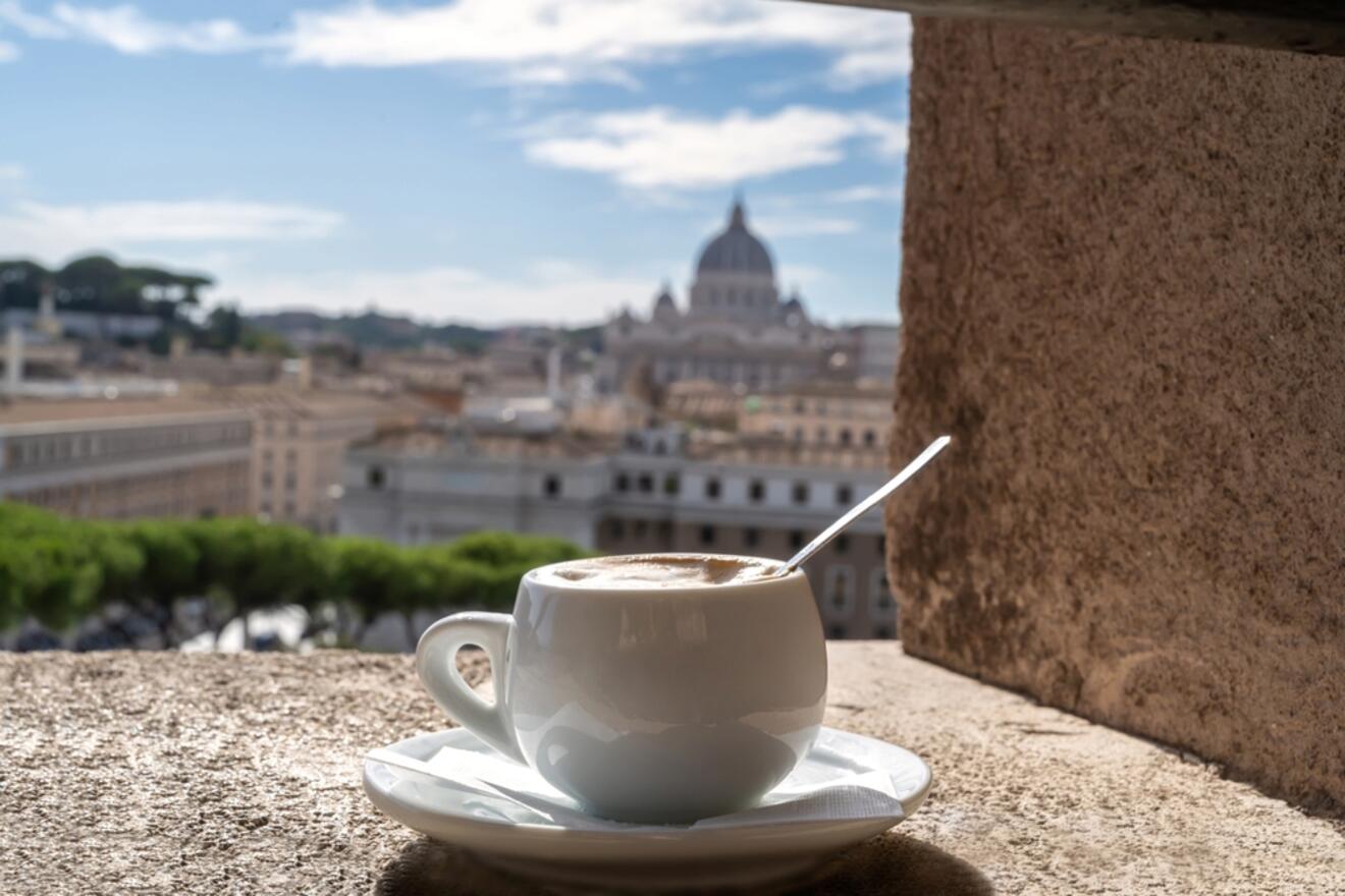 A cup of cappuccino on a ledge with a scenic view of St. Peter's Basilica in the background.