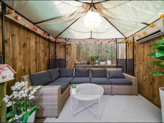 Cozy outdoor lounge area under a canopy with wicker furniture and plants.