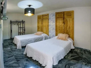 A bedroom with marble floor, featuring two single beds with white bedding, light brown pillows, a black ceiling light, wooden panel walls, and a black metal clothes rack.