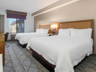 A hotel room with two queen-sized beds, a window with a view, a work desk, and modern lighting.