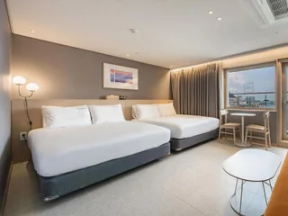 Hotel room with two double beds, a window view, and minimalist decor.