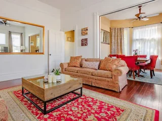 An elegant living room featuring a plush sofa, a decorative red rug, a wooden coffee table, and an adjacent dining area.