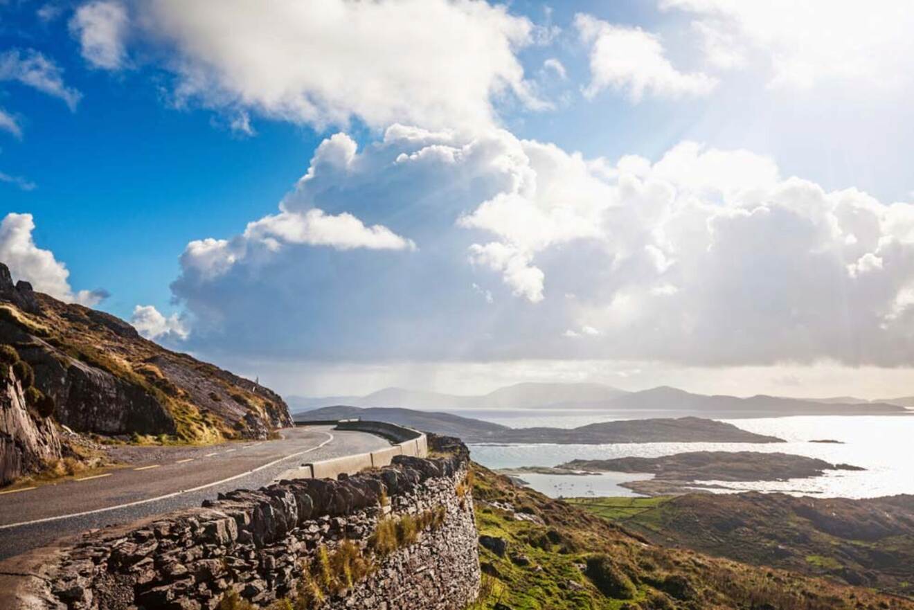 Scenic coastal road on the Ring of Kerry, Ireland, with a winding path and dramatic cloudy skies over the ocean.