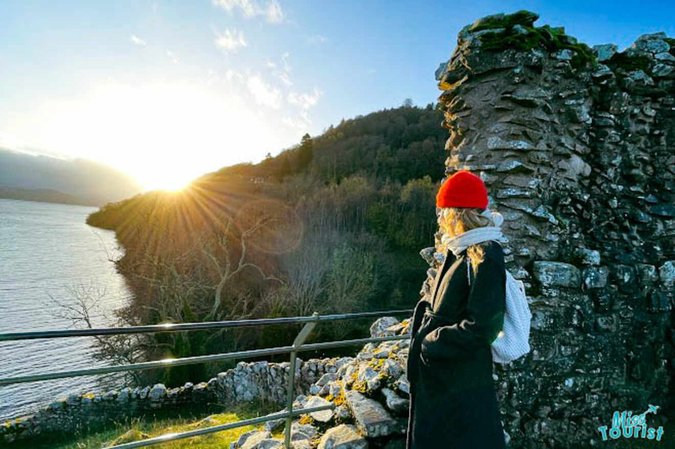 The writer of the post wearing a red beanie and dark coat, gazing at the sunset over a scenic view of Urquhart Castle and Loch Ness in Inverness.