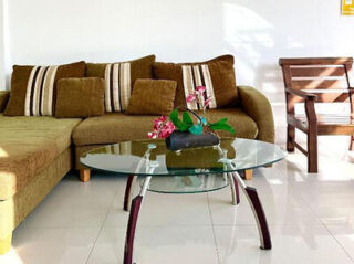 Modern living room with a brown sectional sofa, striped cushions, a round glass coffee table with a floral arrangement, and a wooden chair.
