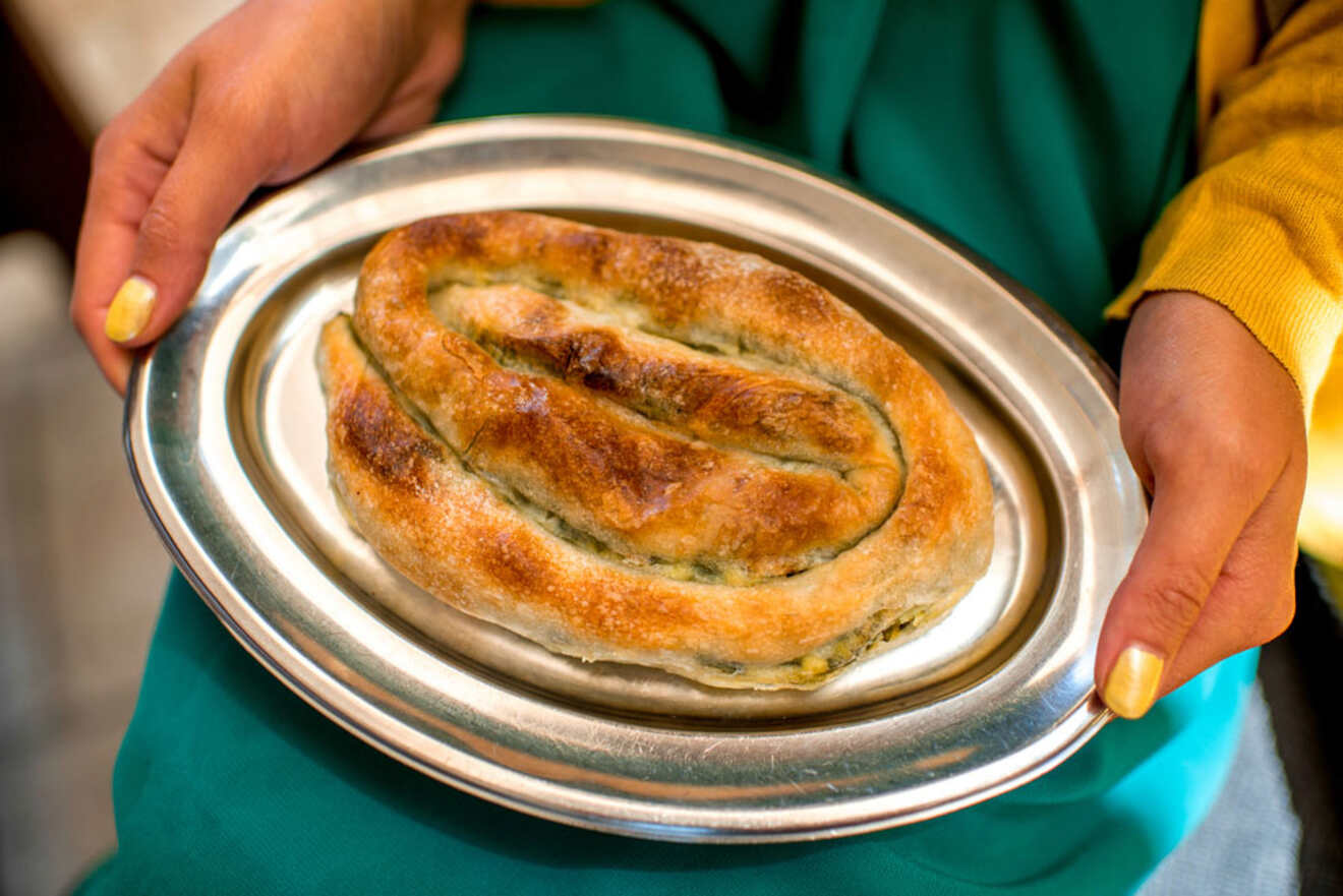 Close-up of a person holding a silver tray with a freshly baked Burek, a traditional Albanian pastry.