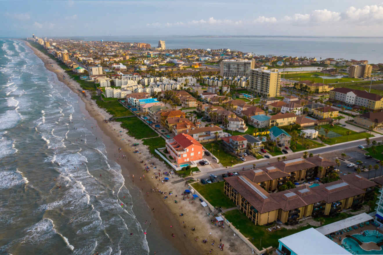 Aerial view of a coastal city with numerous colorful buildings and hotels along a sandy beach, with waves crashing onto the shore and people scattered along the beach.