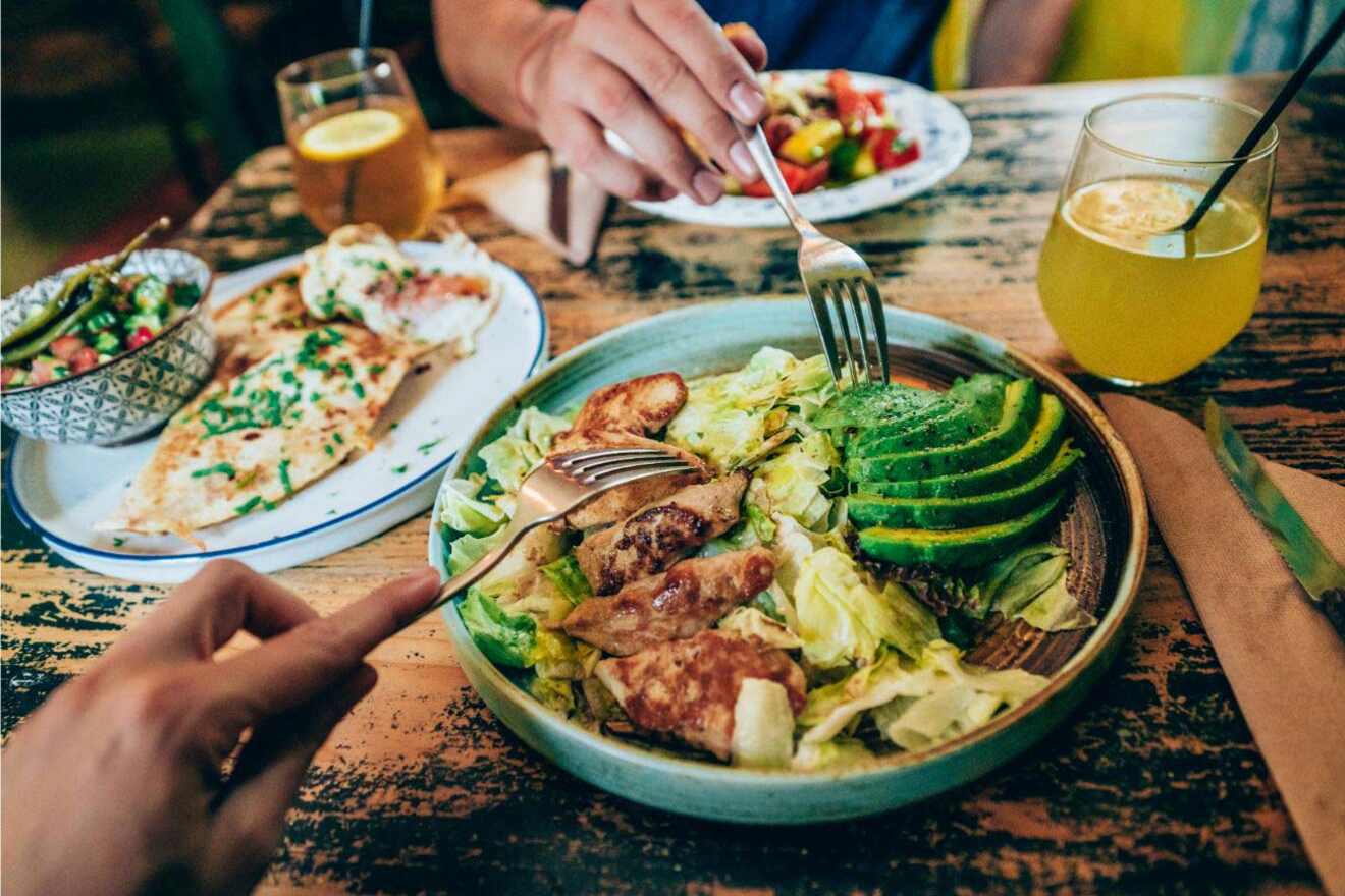 A table set with a variety of healthy dishes, including a salad with avocado and chicken.