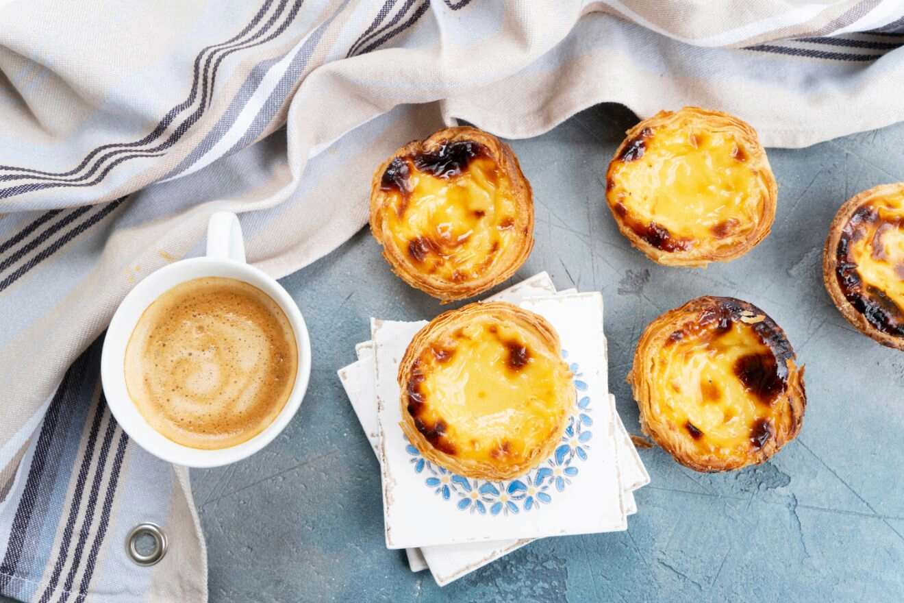 Portuguese custard tarts (Pastel de Nata) and a cup of coffee on a rustic blue tablecloth.