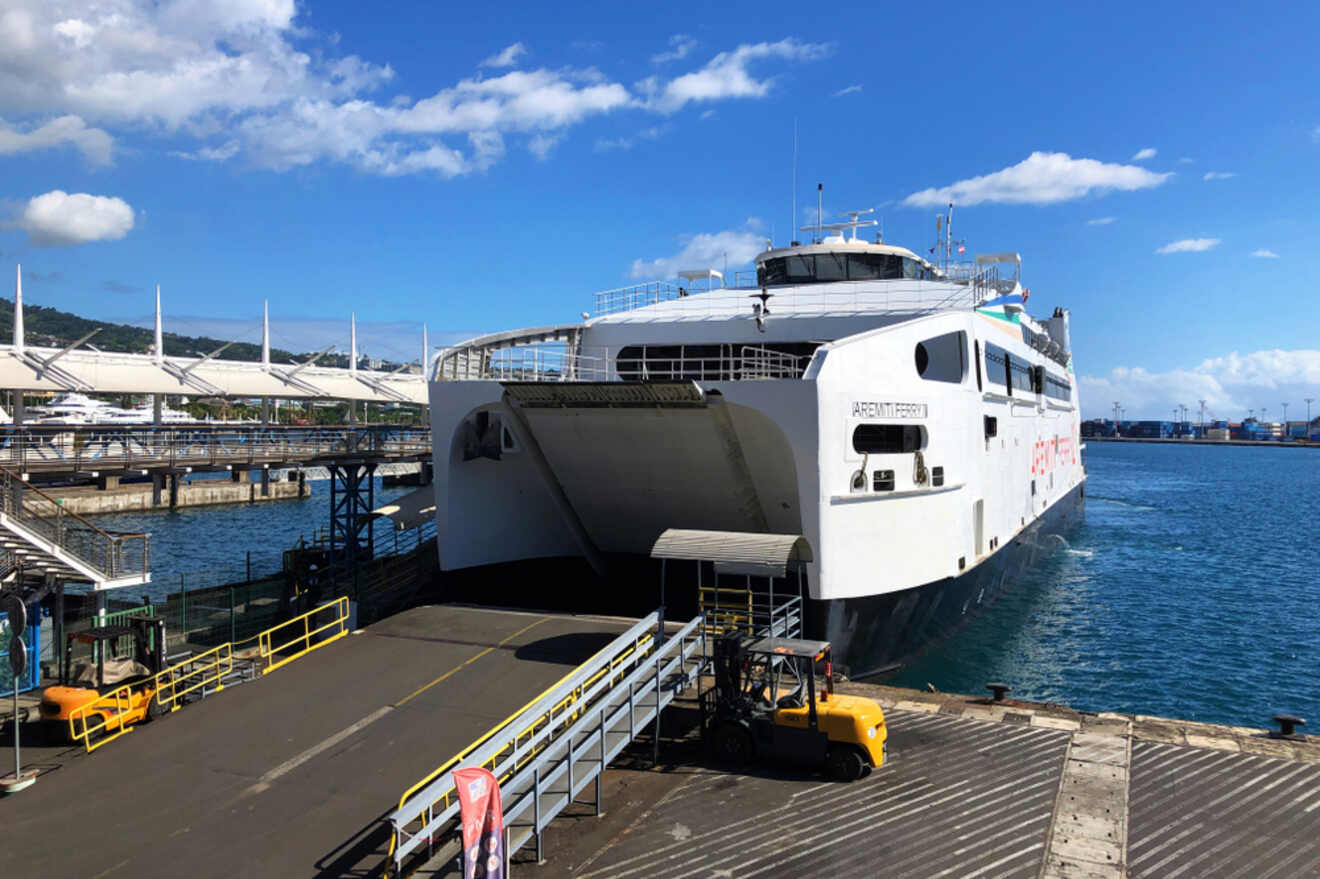 A white Toyota Land Cruiser driving off the Terevau ferry onto a dock, with the red ferry in the background.