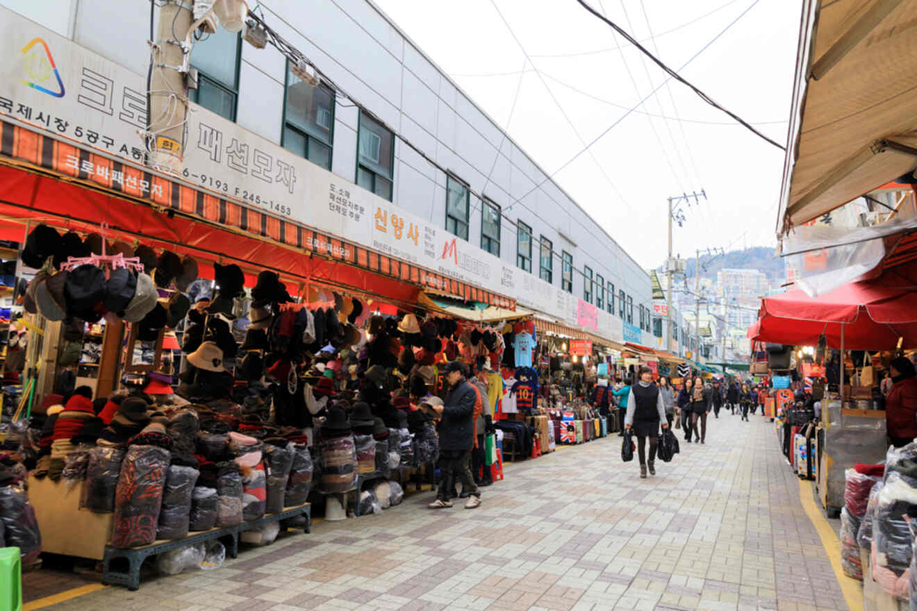 Bustling outdoor market with stalls selling various goods and shoppers walking along the street.