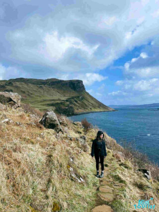 The writer of the post hiking along a coastal path on the Isle of Skye, with rolling hills and the sea in the background.