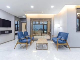Spacious living room with blue chairs, a coffee table, and large windows.