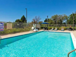 An outdoor swimming pool with lounge chairs and umbrellas, set against a clear blue sky.