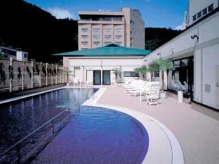 An outdoor pool area with lounge chairs, surrounded by buildings and a scenic mountain backdrop.