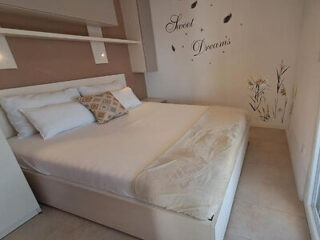 A neatly made bed with white bedding and multiple pillows in a bright room. “Sweet Dreams” and decorative decals are on the wall above the bed.