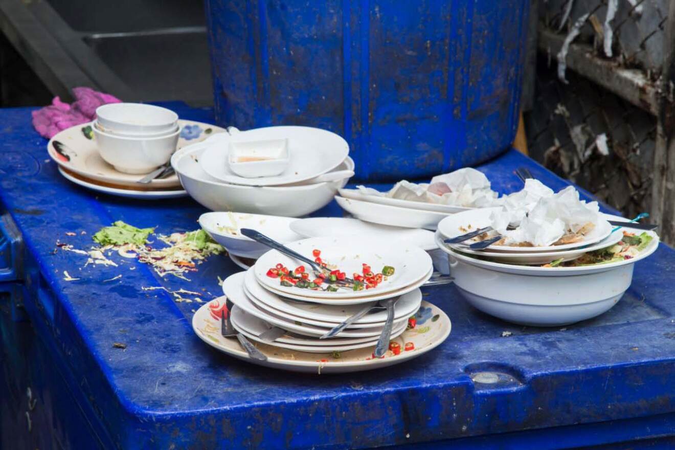 Dirty plates with leftover food stacked near a trash bin.