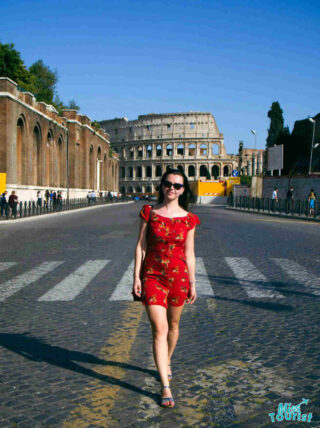 The writer of the post walking on a cobblestone street towards the Colosseum in Rome, wearing a red dress.