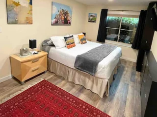 A bedroom featuring a cozy bed with colorful pillows, wooden furniture, and artistic wall decor.