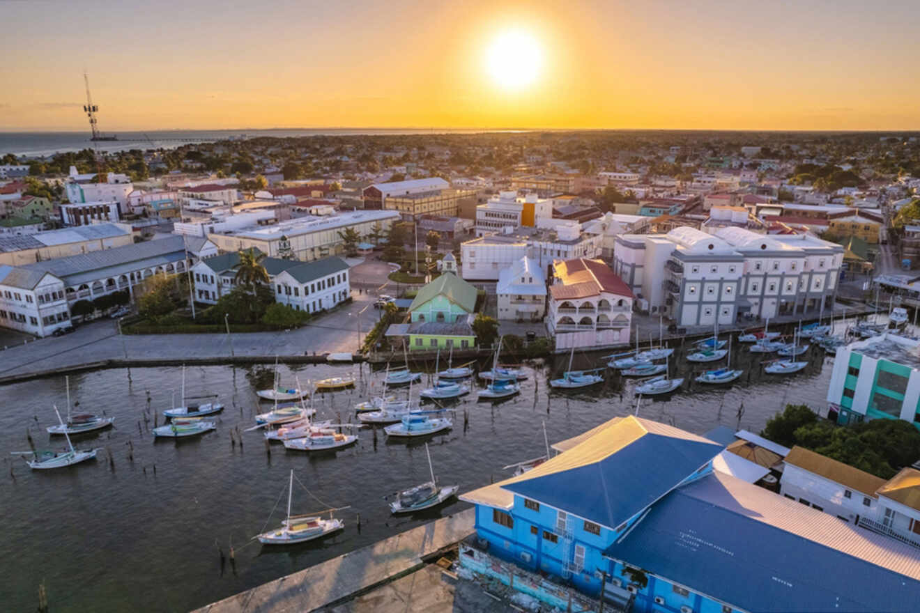 Aerial view of a coastal town with a marina full of boats, buildings, and the sun setting on the horizon.