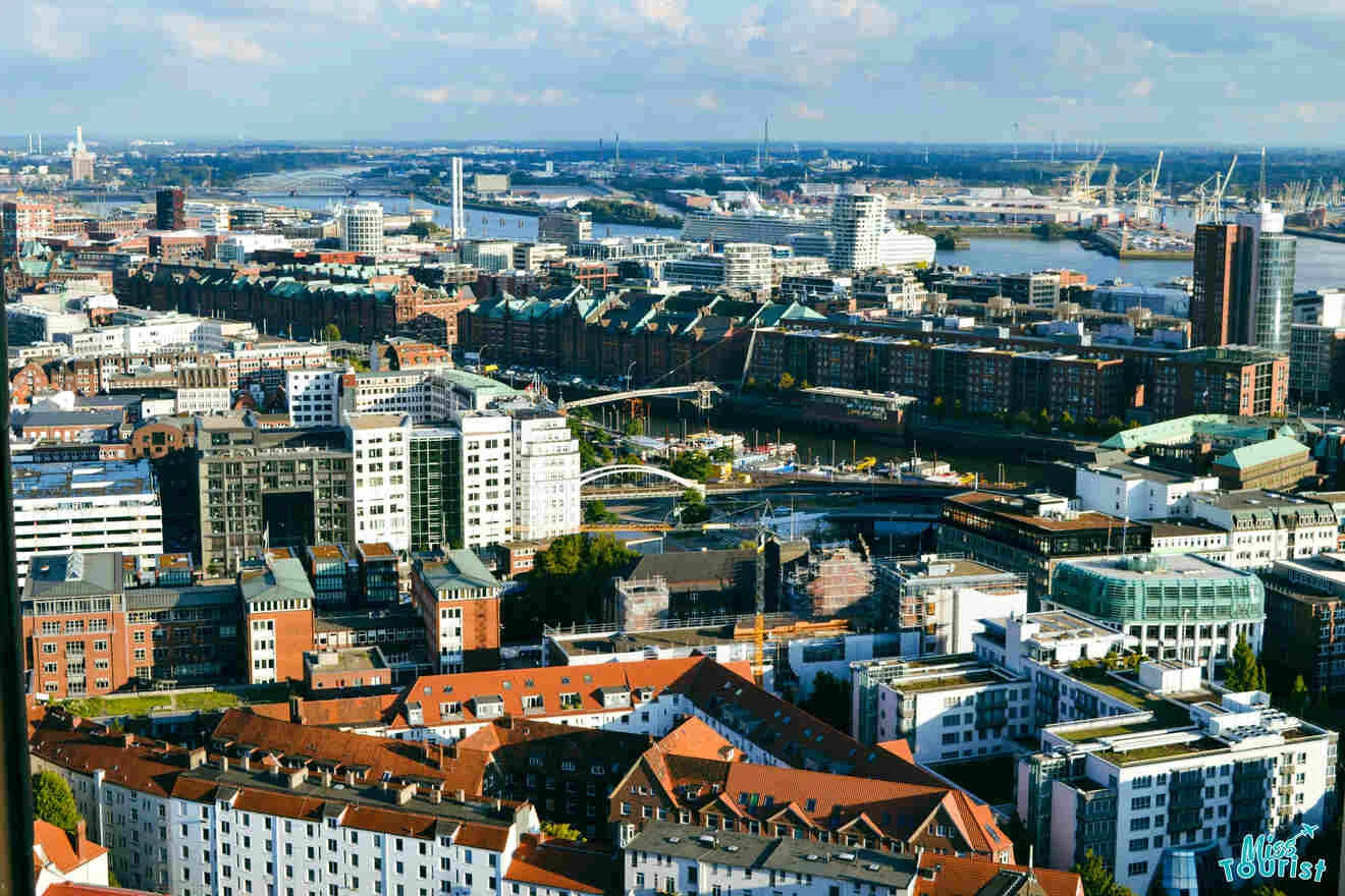 Aerial view of a cityscape featuring dense urban buildings, a river with docked ships, and a mix of residential and commercial areas under a blue sky.